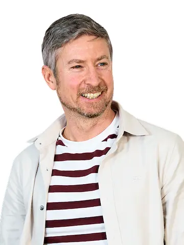 A smiling man wearing a striped T-shirt under a white jacket.