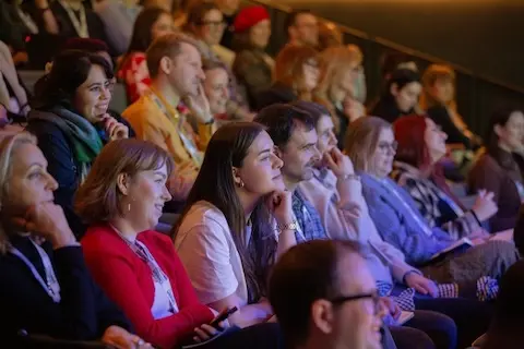 Rows of attendees in the audience, smiling and enjoying the conference.
